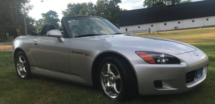 Silver 2002 Honda S2000 roadster with the top down, parked on grass, front three-quarter view