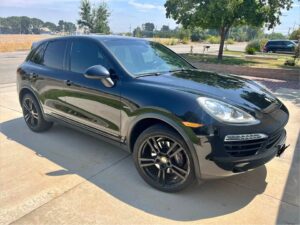Black 2014 Porsche Cayenne Diesel on black wheels in a driveway, front three-quarter view