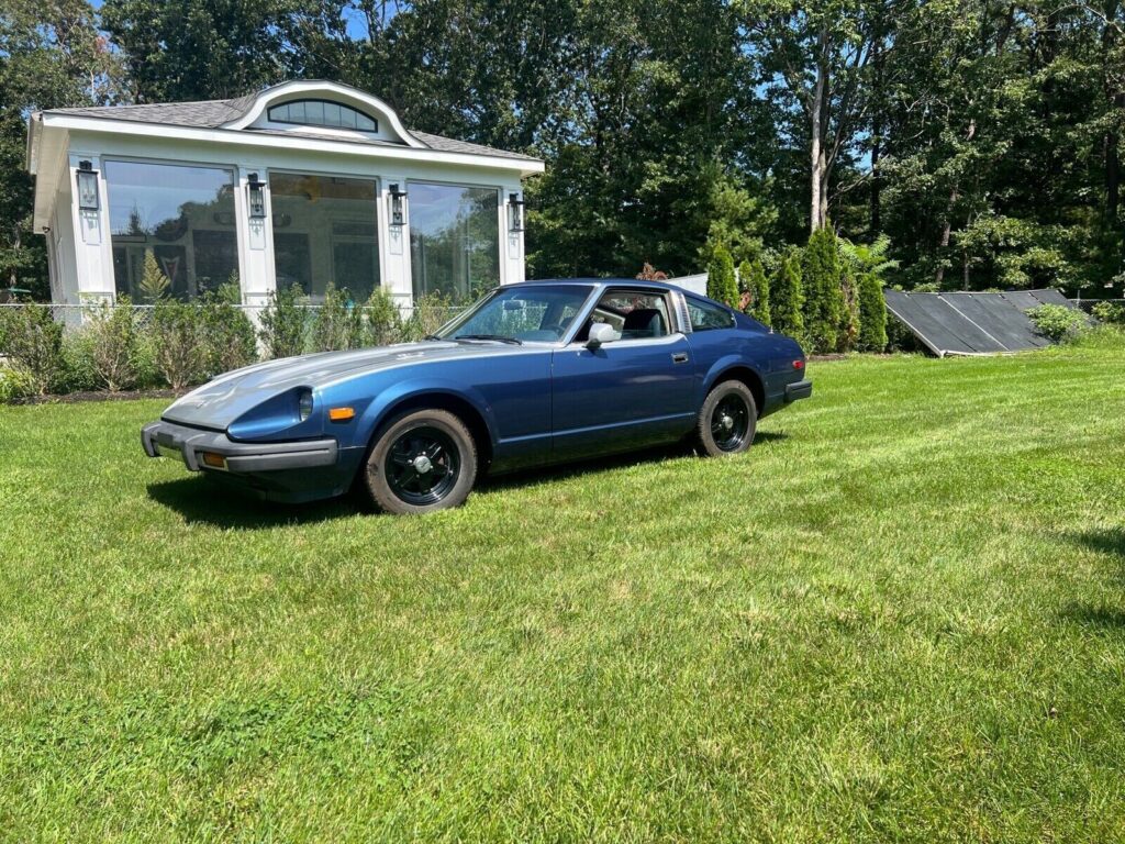 Dark blue 1979 Datsun 280ZX two-seat coupe parked on a lawn in front of a white garden building, front three-quarter view