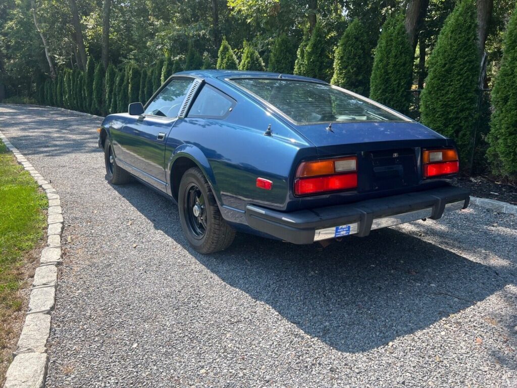 Rear three-quarter view of the dark blue 1979 280ZX on a gravel driveway lined with trees