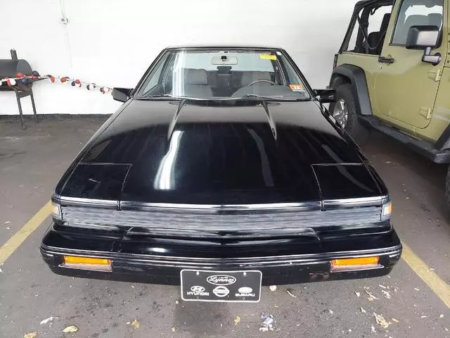 Black 1987 Nissan 200SX XE parked in a garage, straight-on front view with the pop-up headlights closed