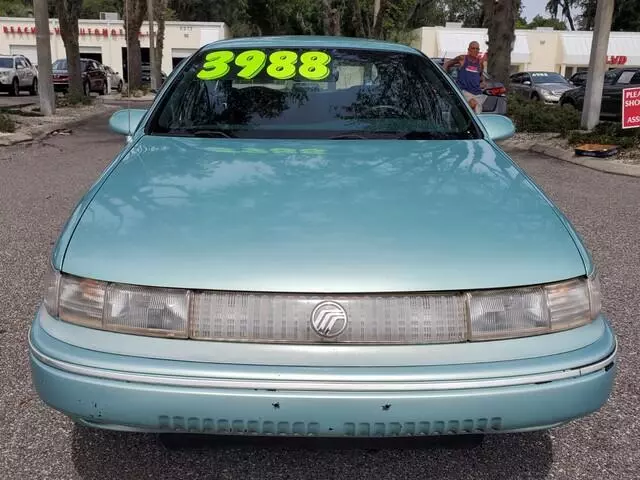 Front view of a light teal 1994 Mercury Sable GS sedan on a dealer lot, with a price written on the windshield