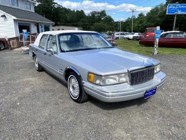 Silver 1992 Lincoln Town Car Signature Series sedan on a gravel dealer lot, front three-quarter view with wire-style wheel covers