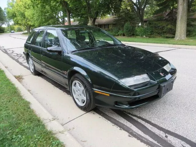 Dark green 1995 Saturn SW2 station wagon parked at a curb on a tree-lined street, front three-quarter view