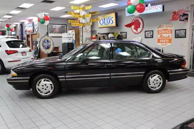 Driver-side profile of the black 1994 Pontiac Bonneville SE four-door sedan in a showroom decorated with vintage signs