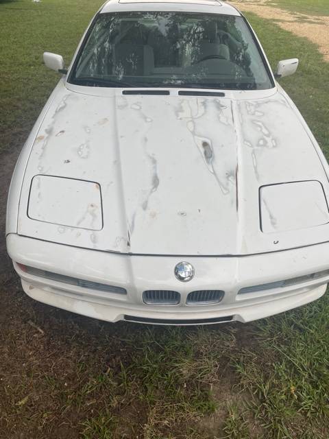 Front view of the white BMW 850i showing its pop-up headlight covers and heavily stained hood