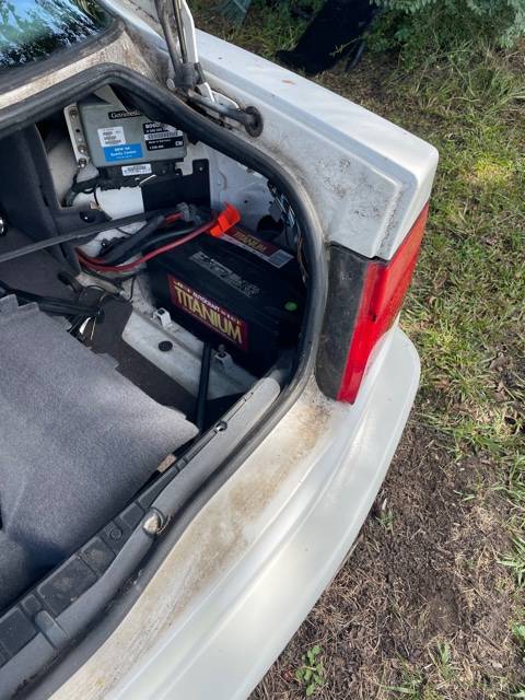 Open trunk of the white BMW 850i showing the battery and electronics mounted on the right side